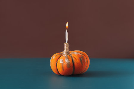 Burning candle in handmade pumpkin against blue-brown background.の写真素材