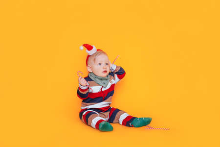Little boy in claus hat holding candy in his hands in front of yellow background.の写真素材