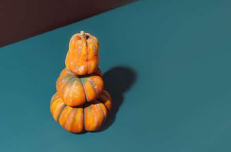 Three handmade pumpkins stand on top of each other against brown and cian background, hard shadows.の写真素材