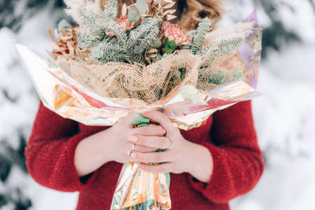 Woman holding a beautiful bouquet of flowers in her hands on a background of snow. Winter time. Gift...