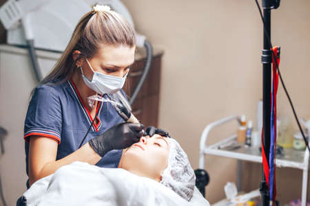 beautician making a permanent make-up procedure on eyebrows using a machine.