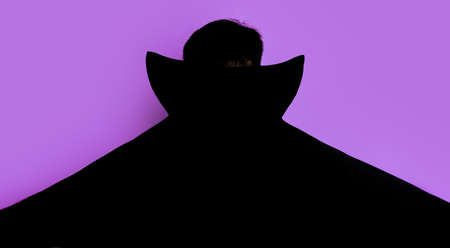 Man in dracula costume stands with his back in black cloak.