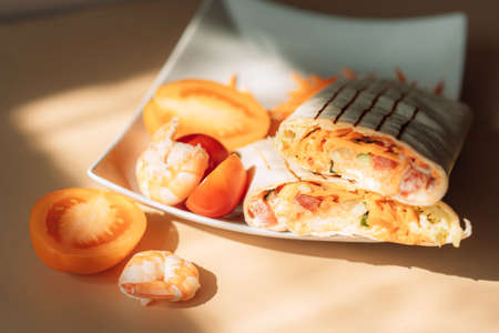 Shawarma cut in half with shrimps and tomato on wooden table.の写真素材
