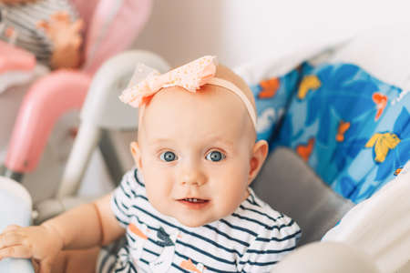 Child in child seat with blue eyes and bow on his head.