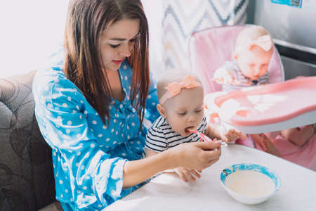 Mom feeds one of the twins from spoon with baby food.の写真素材