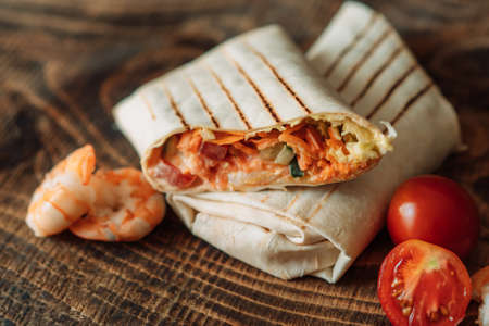 Shawarma cut in half with shrimps and tomato on wooden table.の写真素材