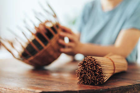 Woman weaves basket of paper tubes on wooden table.の写真素材