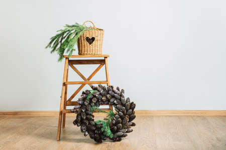 Branch of Christmas tree in wicker basket and wreath of cones on wooden stepladder.の写真素材
