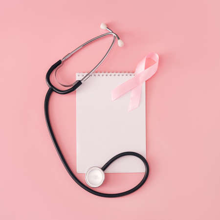 Pink ribbon and stethoscope on white sheet of notepad on pink background.の写真素材