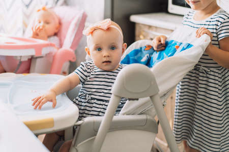 Twins sitting on chairs and older sister.の写真素材
