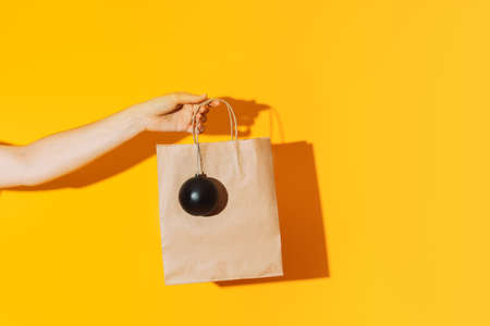 Hand holding paper bag with black matte ball against yellow background.
