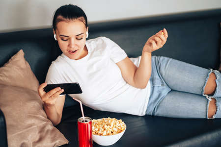Girl watching e-sports stream with can of juice and popcorn.