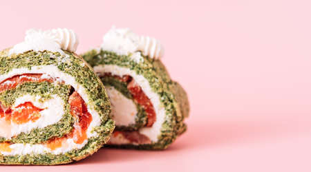 Two wedges of roll with spinach and red fish on pink background.の写真素材