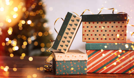 New year holiday boxes are stacked on top of each other next to blurred christmas tree.