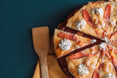 Seafood pizza cut into equal pieces on wooden tray.