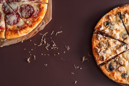One pizza with mushrooms and chicken and another pizza with salami on brown background.の写真素材