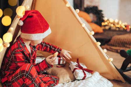 Boy in red pajamas sits next to gifts and eats cookieの写真素材