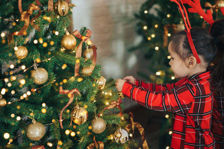 Girl in pajamas hangs bauble on Christmas treeの写真素材