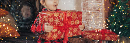 Surprised girl in red pajamas hugs large box with gift.の写真素材