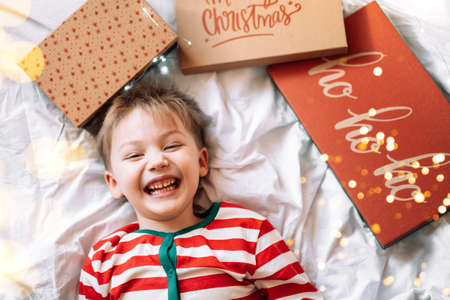 Boy lies on the bed with covers from gift boxes and garland.の写真素材