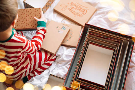 Child in striped pajamas standing next to open boxes on white bed.の写真素材