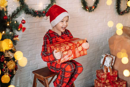 Boy in pajamas and santa hat on his head holding big gift.の写真素材
