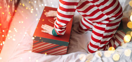 Child in striped pajamas closes gift box on white bed with superimposed lights.の写真素材
