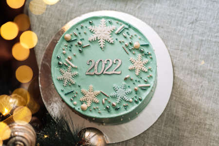 Turquoise Christmas cake with 2022 lettering next to decorated Christmas tree.の写真素材