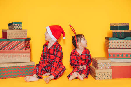 Brother and sister in pajamas sit with gifts on yellow background.の写真素材