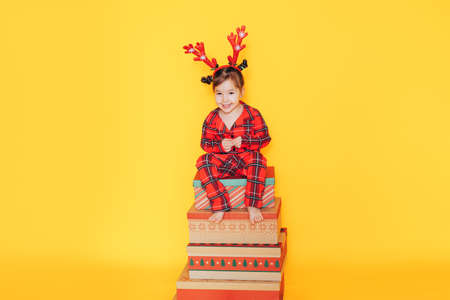 Girl in red pajamas sitting on gift boxes against yellow background.の写真素材