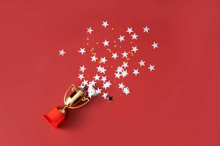 Stars fly out of the gold-colored victory cup on red background.の写真素材