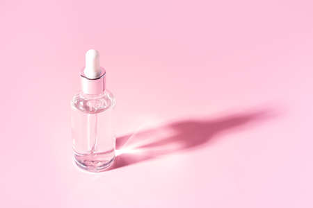 Glass jar with pipette of transparent liquid on pink background.の写真素材
