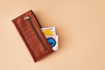 Two blue and yellow condoms sticking out of wallet on beige backgroundの写真素材