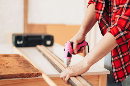 Girl in red plaid shirt drills board with small drillの写真素材