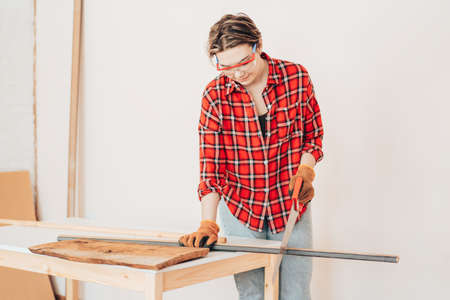 Laborer girl sawing wooden block with hand sawの写真素材