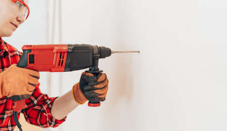 Laborer girl in protective gloves drills concrete wall with drillの写真素材