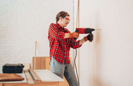 Laborer girl in protective glasses drills concrete wall with drillの写真素材
