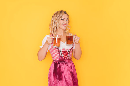 Woman in festive german dress holding two mugs with beer in front of yellow backgroundの写真素材