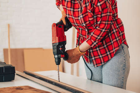Laborer girl drilling plank with drill on the tableの写真素材