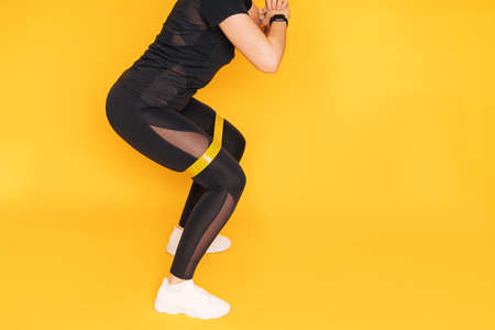Girl crouches with an elastic band on her legs against yellow background