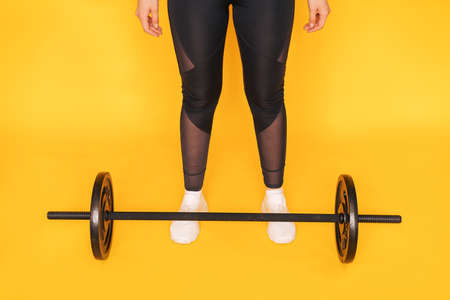 The girl stands next to the barbell against yellow backgroundの写真素材