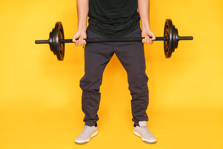 Guy holds barbell in his hands against yellow backgroundの写真素材