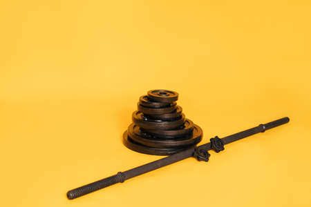 Stack of discs of different weights next to the bar against yellow backgroundの写真素材