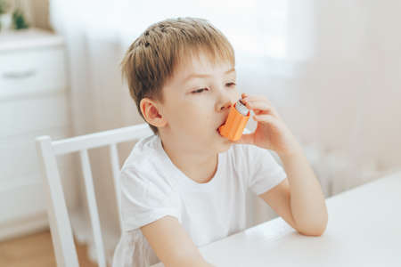Little boy uses an asthma inhaler while sitting at tableの写真素材