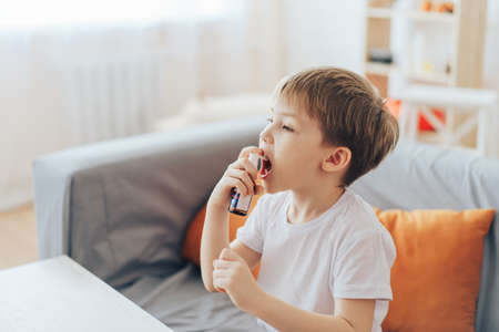 Little boy uses throat spray while sitting on the couchの写真素材