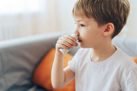 Little boy uses hormonal nasal spray while sitting on the couchの写真素材