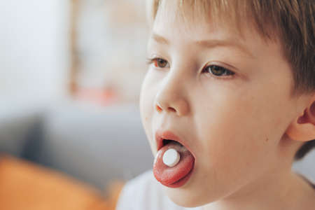 Little boy holds white round pill on his tongueの写真素材