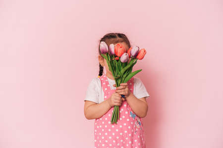 Little girl with bouquet of tulips against pink background happy mothers day,