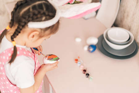 Child in bunny ears prepares colored eggs for Easterの写真素材