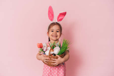 Basket with eggs and flowers in the hands of girl against pink backgroundの写真素材